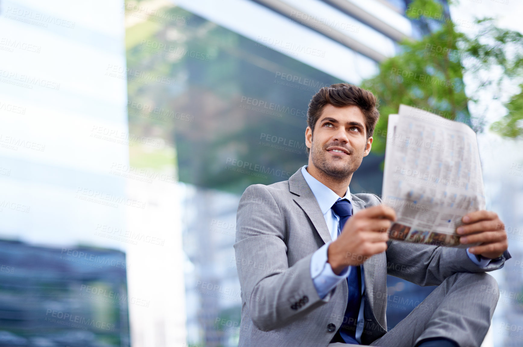 Buy stock photo A handsome young businessman reading a newspaper in the city