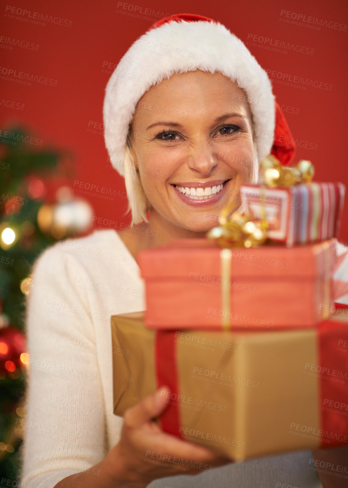 Buy stock photo Christmas, present and woman in portrait for holiday, celebration and tradition on a red or wall background. Excited, happy and young person by tree with bokeh lights, gift or giving box at home