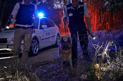 Buy stock photo Shot of two policemen and their canine tracking a suspect through the brush at night