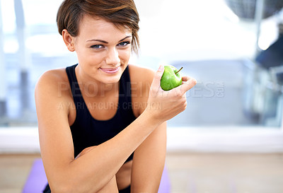 Buy stock photo Shot of a sporty young woman sitting on a gym floor eating an apple