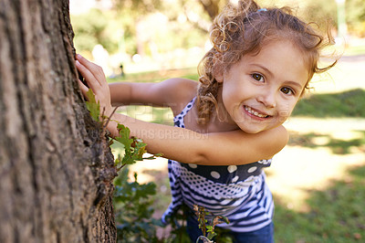 Buy stock photo Portrait of a little girl hiding behind a tree in a park