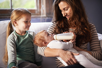 Buy stock photo Shot of a baby being fed by her mother while her sister watches