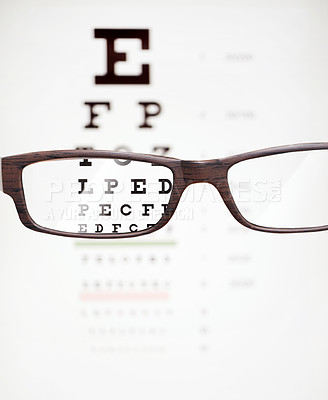 Buy stock photo A cropped shot of eyeglasses in front of a snellen chart