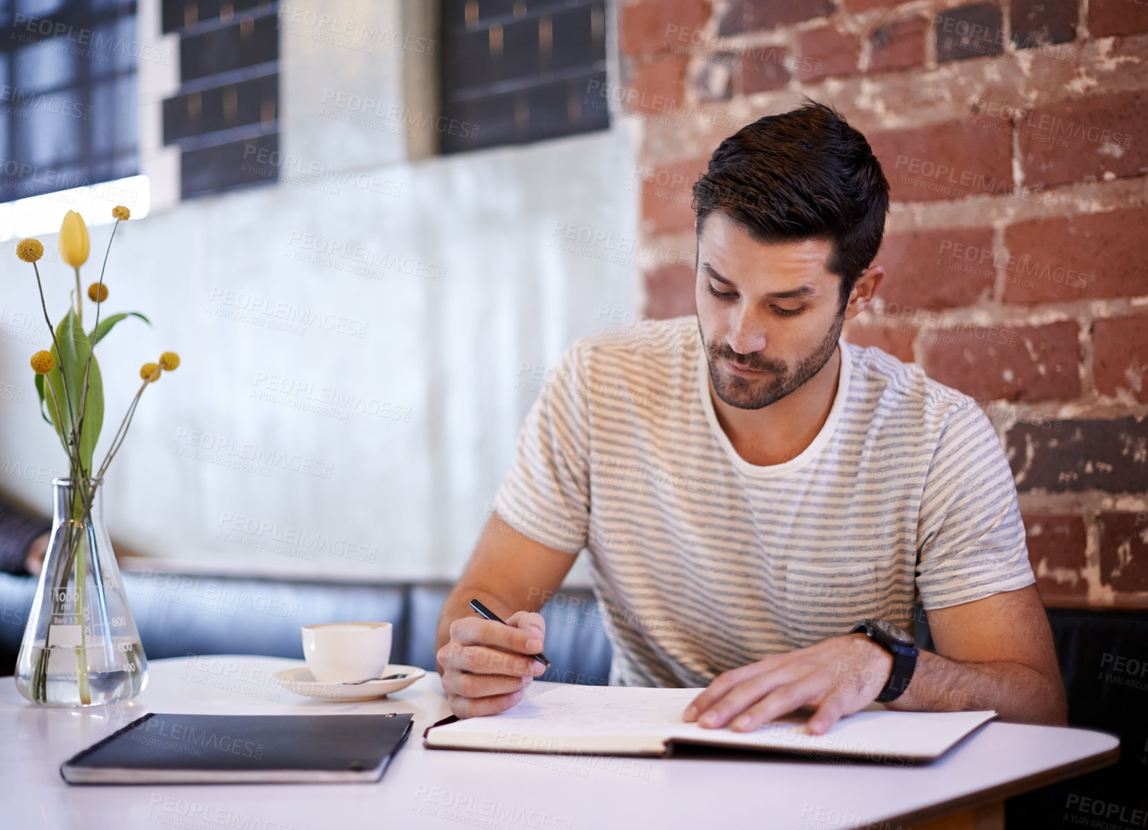 Buy stock photo Shot of a handsome young man writing in a notebook while sitting at a restaurant table