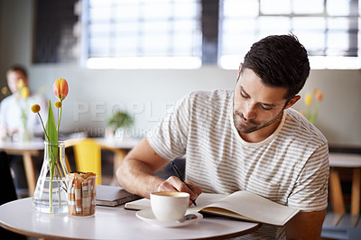 Buy stock photo Shot of a handsome young man writing in a notebook while sitting at a restaurant table