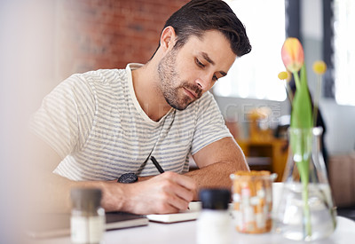 Buy stock photo Shot of a handsome young man writing in a notebook while sitting at a restaurant table