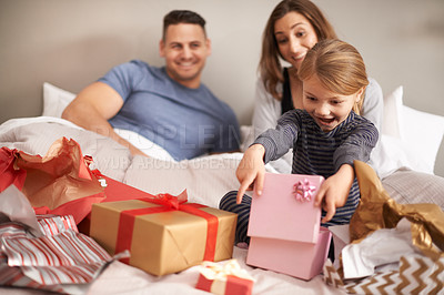 Buy stock photo Shot of a little girl opening presents in bed as her parents watch