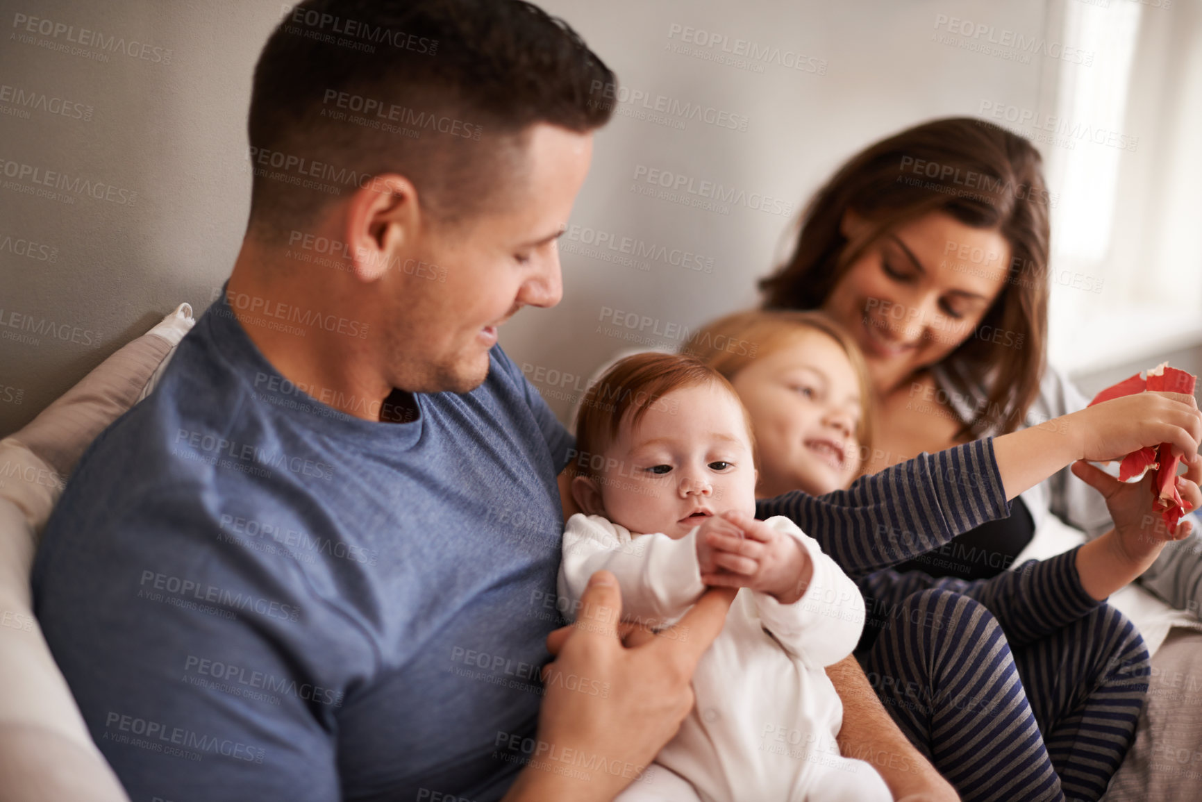 Buy stock photo Shot of an affectionate young family lying in bed and exchanging gifts