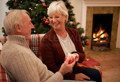 Buy stock photo Christmas, gift and love with a senior couple in celebration while sitting in the living room of their home together. Tradition, present and bonding with a mature man and woman in the festive season
