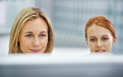 Buy stock photo Shot of two attractive female colleagues behind a computer screen in the office