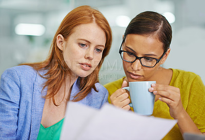 Buy stock photo Two attractive female colleagues looking over some work together in the office
