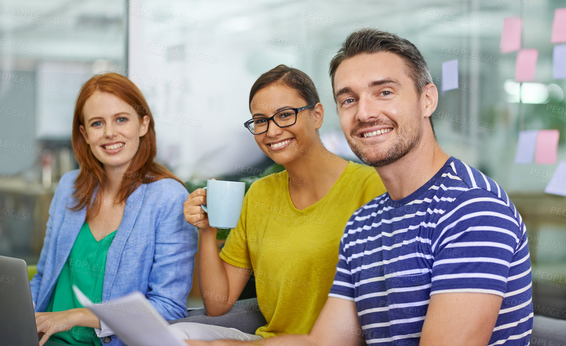 Buy stock photo Three colleagues sitting together having coffee over work documents in the office