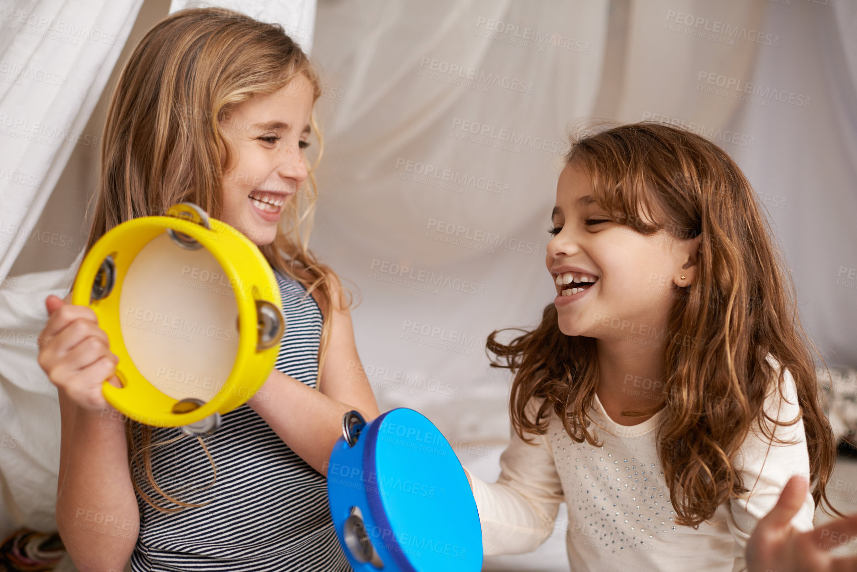 Buy stock photo Shot of two cute little girls playing with tambourines at home