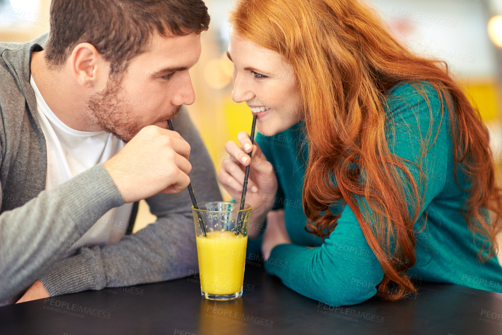Buy stock photo Cropped shot of a happy young couple sharing a glass of juice on a date at a cafe