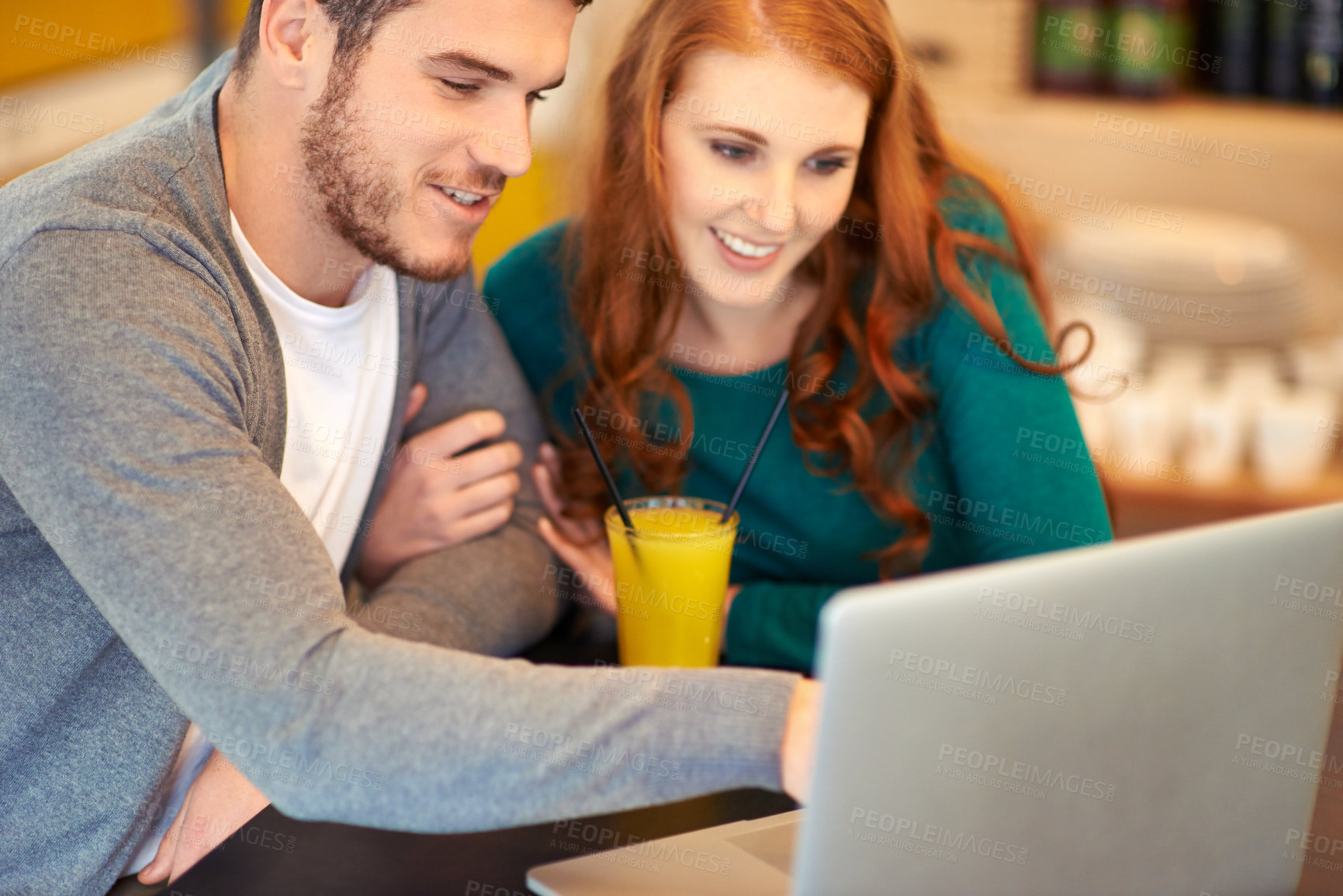 Buy stock photo Shot of a young couple using a laptop while having a drink at a cafe