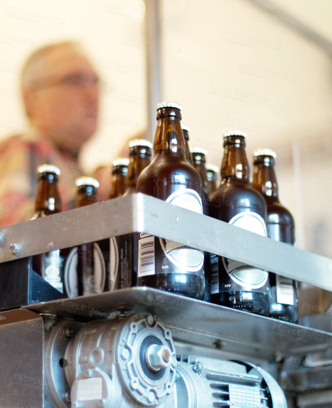 Buy stock photo Shot of a batch of bottled beer in a brewery with an employee in the background