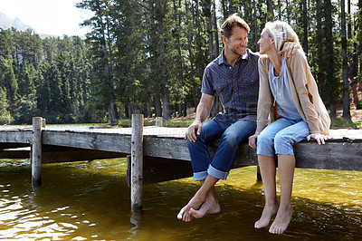 Buy stock photo Couple, lake and sitting on jetty, outdoor and happy for hug on vacation, relax or nature in summer. Man, woman and embrace with smile, care or bonding with connection for love on holiday in Colorado