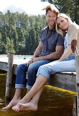 Buy stock photo Shot of a loving mature couple sitting on a pier out on a lake in the countryside