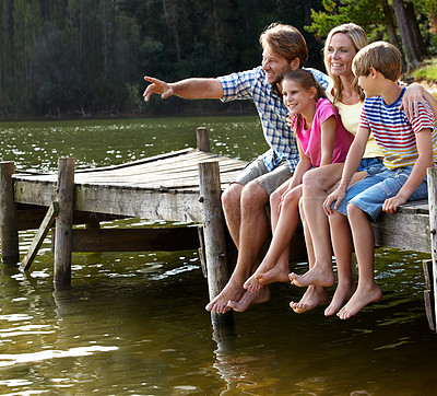 Buy stock photo Shot of a loving family sitting on a pier out on a lake in the countryside