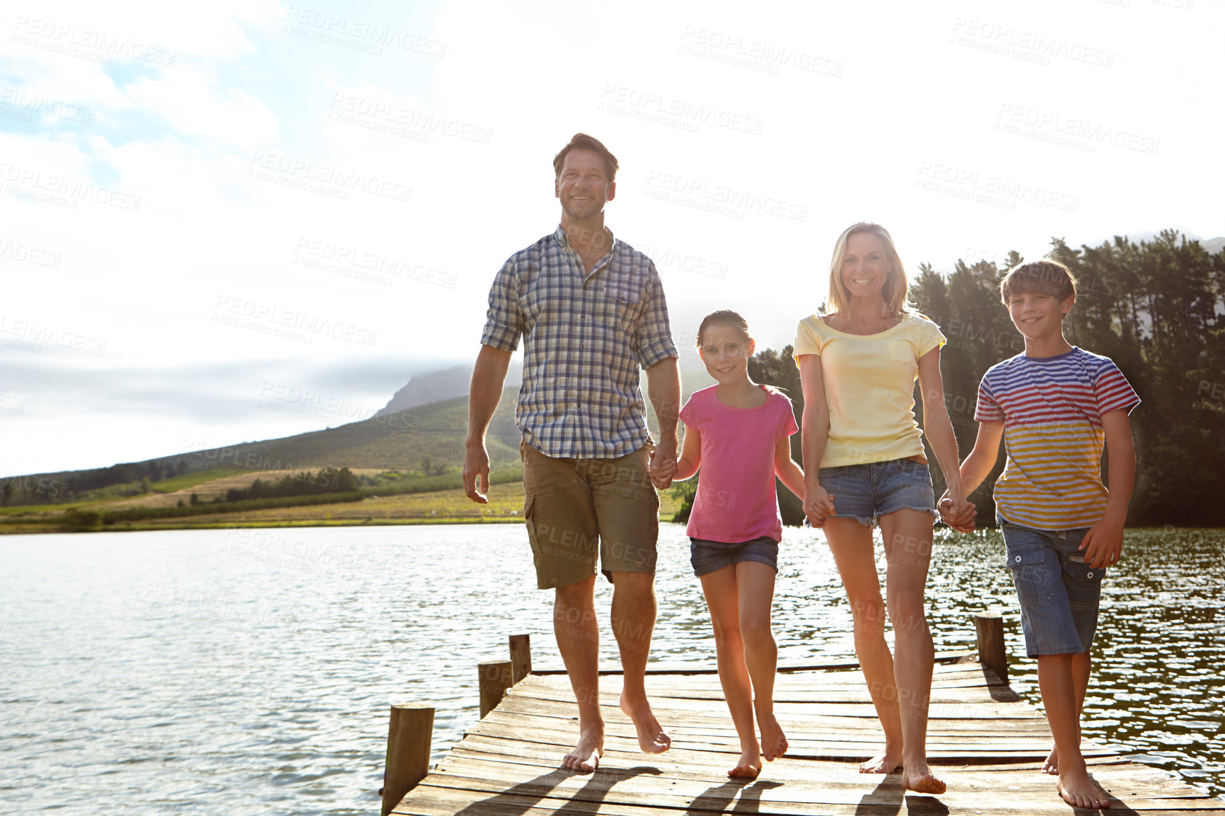 Buy stock photo Family, children and pier by lake for holding hands in portrait, happy or vacation with love in summer sunshine. Mom, dad and kids with smile, care or bonding on walk by river for holiday in Colorado