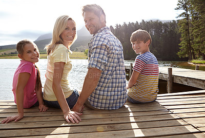 Buy stock photo Parents, lake and children on pier for portrait, happy and sitting on vacation with love in summer sunshine. Mom, dad and kids with smile, care or bonding with family by river on holiday in Colorado