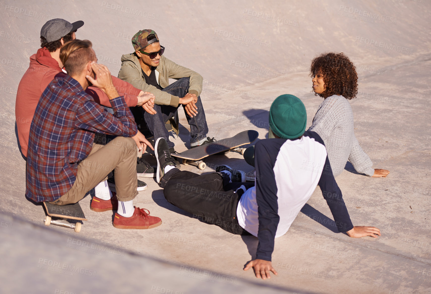 Buy stock photo Shot of a group of friends sitting in the sun at a skate park