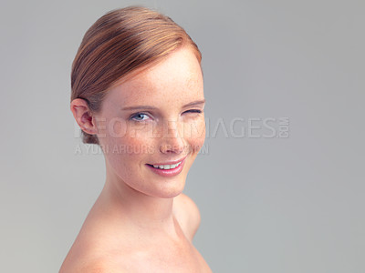 Buy stock photo Portrait, wink and skincare of happy woman for beauty, shine or mockup space in studio isolated on a gray background. Face, smile and ginger model with cosmetics, makeup or treatment for dermatology