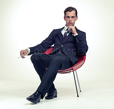 Buy stock photo Suit, smoking and man portrait in chair, studio and serious in formal fashion by white background. Young model, face and elegant clothes with cigarette in armchair and confident in tuxedo by party