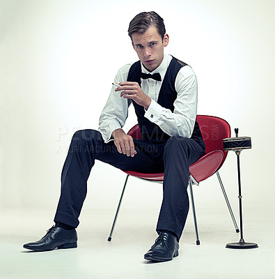 Buy stock photo Smoking, tuxedo and portrait of man in studio with red chair and cigarette for elegant and fancy outfit. Serious, handsome and male model with bowtie and suit for classy fashion by white background.