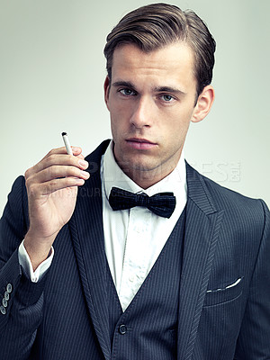 Buy stock photo Portrait, elegant or young gentleman smoking a cigarette in studio, confidence or vintage fashion by white background. Face, serious and man in retro suit or tuxedo, bow tie and class at formal event