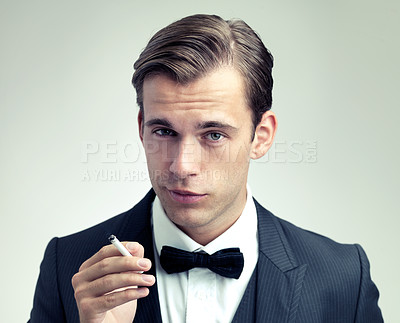 Buy stock photo Portrait, elegant or young man smoking a cigarette in studio, formal or vintage fashion by white background. Face, attitude or gentleman in retro suit or tuxedo, bow tie or habit of tobacco at event