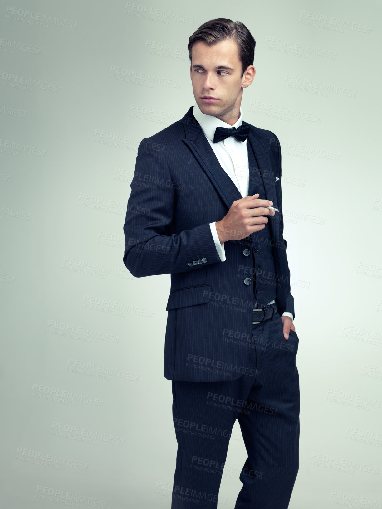 Buy stock photo Thinking, elegant or young gentleman smoking a cigarette in studio, confidence or vintage fashion by white background. Serious, man and idea in retro suit or tuxedo, bow tie and class at formal event