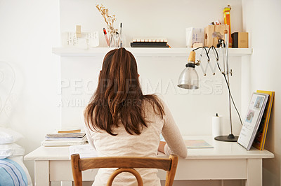 Buy stock photo Rear view shot of a young woman studying at her desk at home