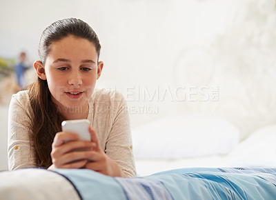 Buy stock photo Shot of a teenage girl lying on her bed and texting on her phone