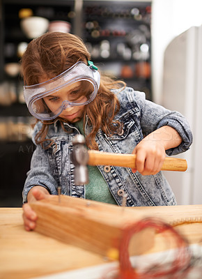 Buy stock photo Chilld, construction and hammer a nail in workshop, play and game in kitchen of home. Female person, girl and safety glasses or tool for wood project or hobby, carpentry and remodeling or manufacture