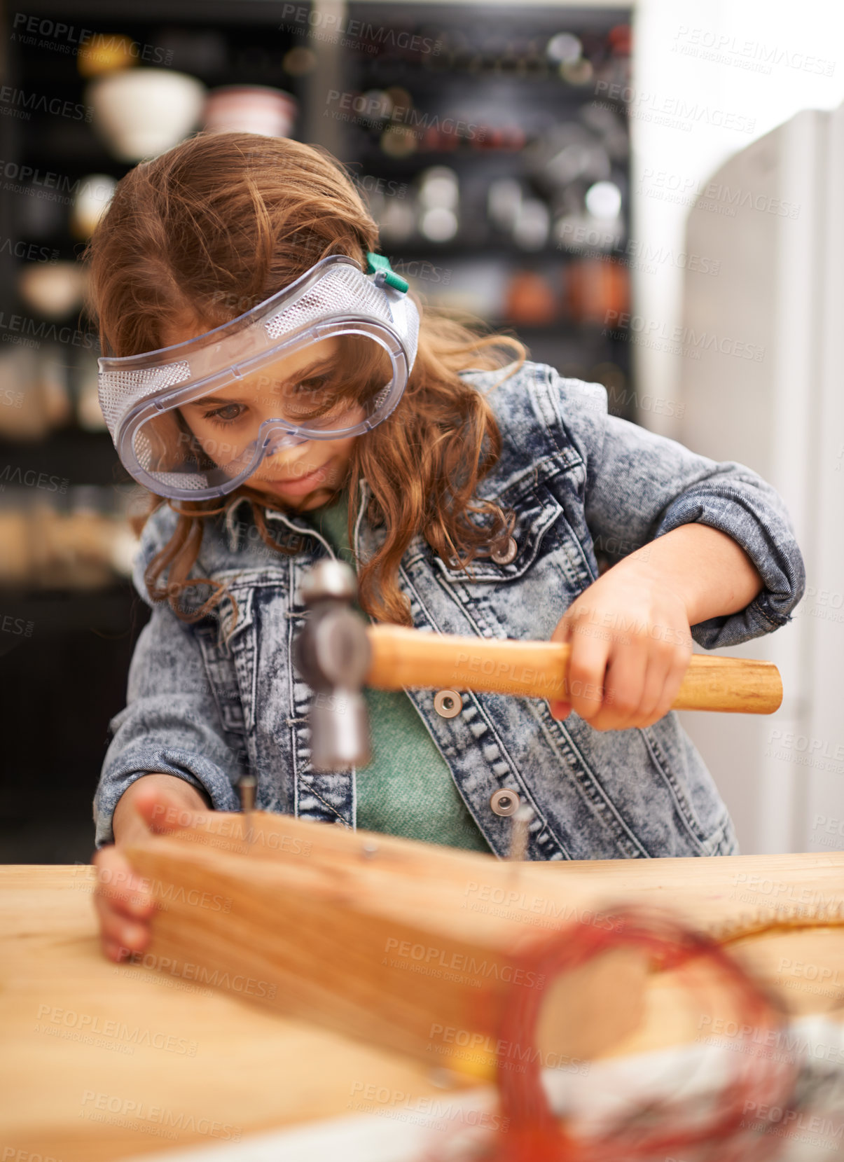 Buy stock photo Chilld, construction and hammer a nail in workshop, play and game in kitchen of home. Female person, girl and safety glasses or tool for wood project or hobby, carpentry and remodeling or manufacture