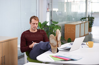 Buy stock photo Office, man and relax at desk with notes from laptop for research work for project or task, feet on table and writing on notepad. Person, computer and online information for creative company
