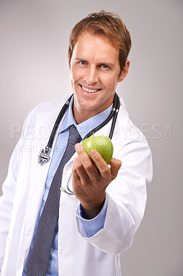 Buy stock photo Studio portrait of a handsome young doctor holding out a green apple
