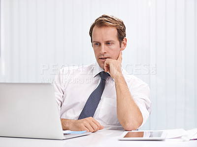Buy stock photo Shot of a young businessman sitting at his desk working on his laptop