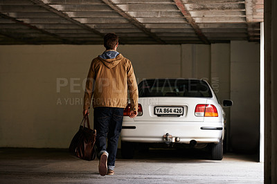 Buy stock photo Rearview shot of a young man walking towards a car in a garage