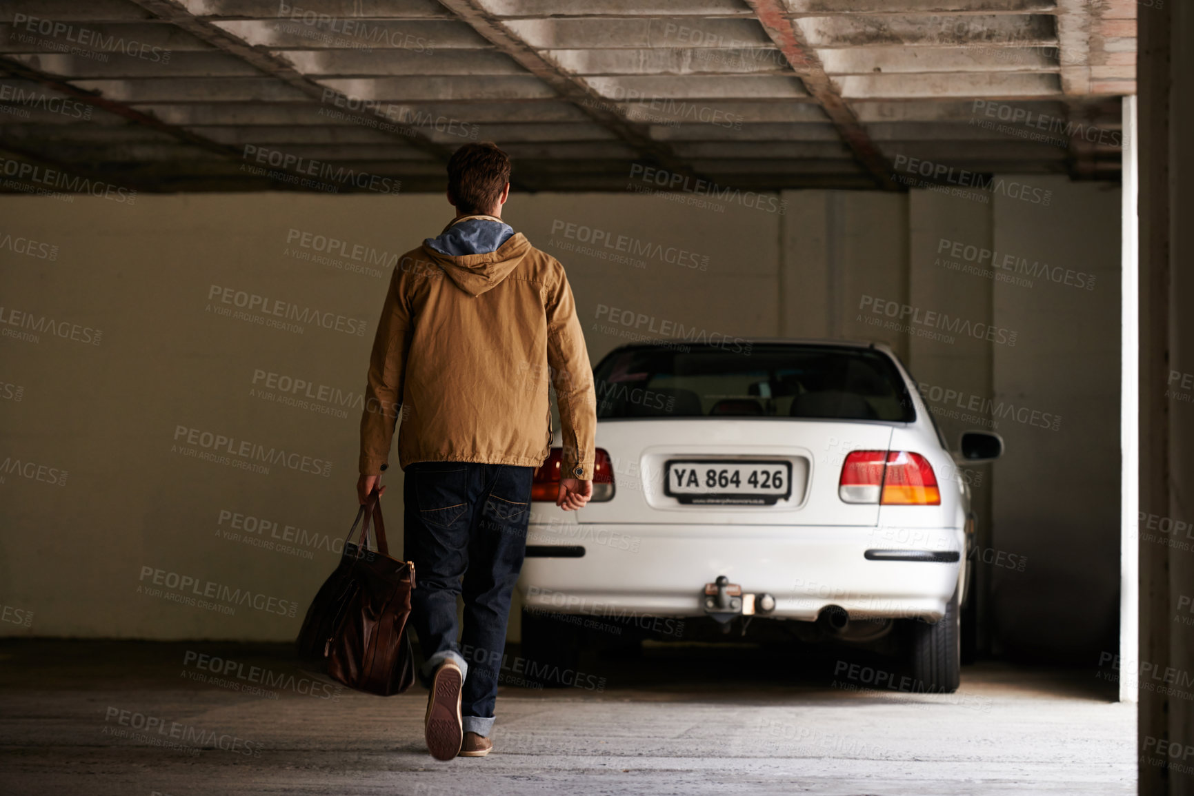 Buy stock photo Rearview shot of a young man walking towards a car in a garage