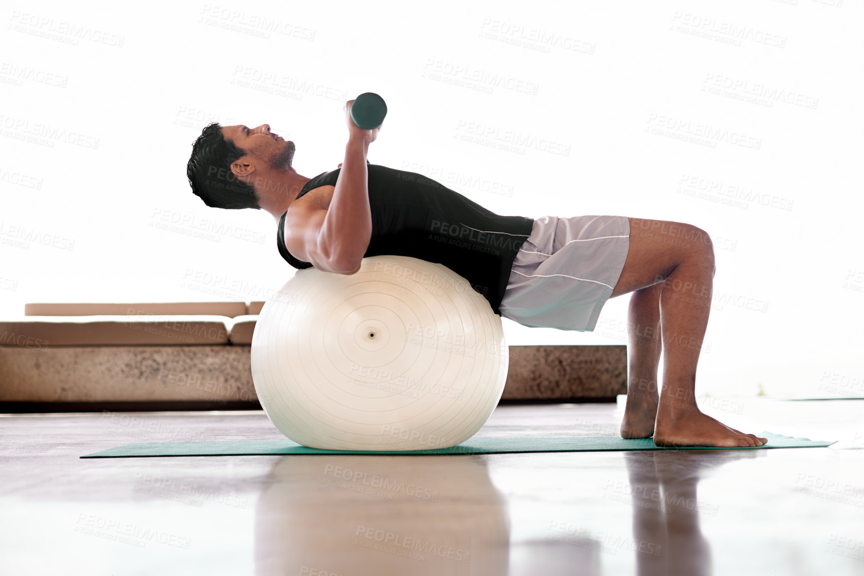 Buy stock photo Full length shot of a man lifting weights while lying on an exercise ball