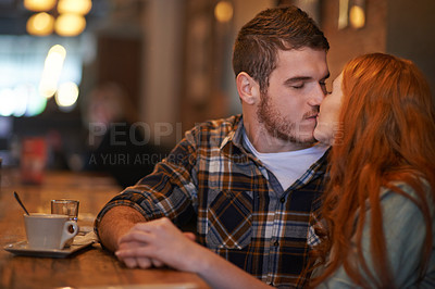 Buy stock photo Shot of an affectionate young couple sharing a kiss while on a coffee date