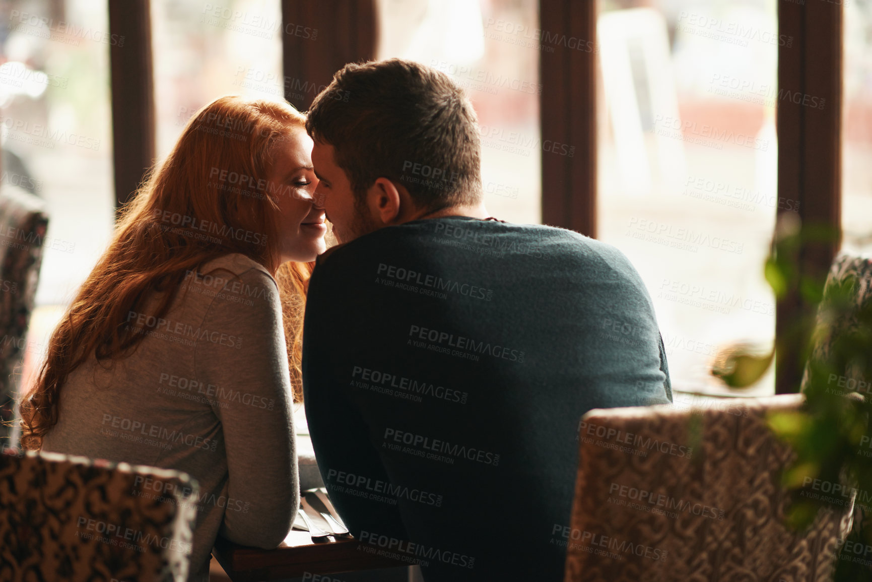 Buy stock photo Couple, happiness and kiss on date at restaurant for bonding, romance or healthy relationship with rear view. Man, woman and affection at coffee shop with smile, trust or love on anniversary vacation