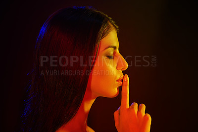 Buy stock photo Studio shot of a beautiful young woman with her finger on her lips in artistic lighting