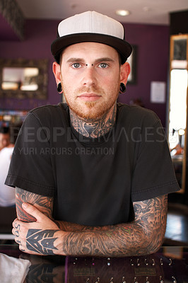 Buy stock photo Tattoos, creative and portrait of a man with tattoos standing by the counter of his artistic studio. Confident, cool and punk man with a edgy, funky and body art or ink creativity business store.
