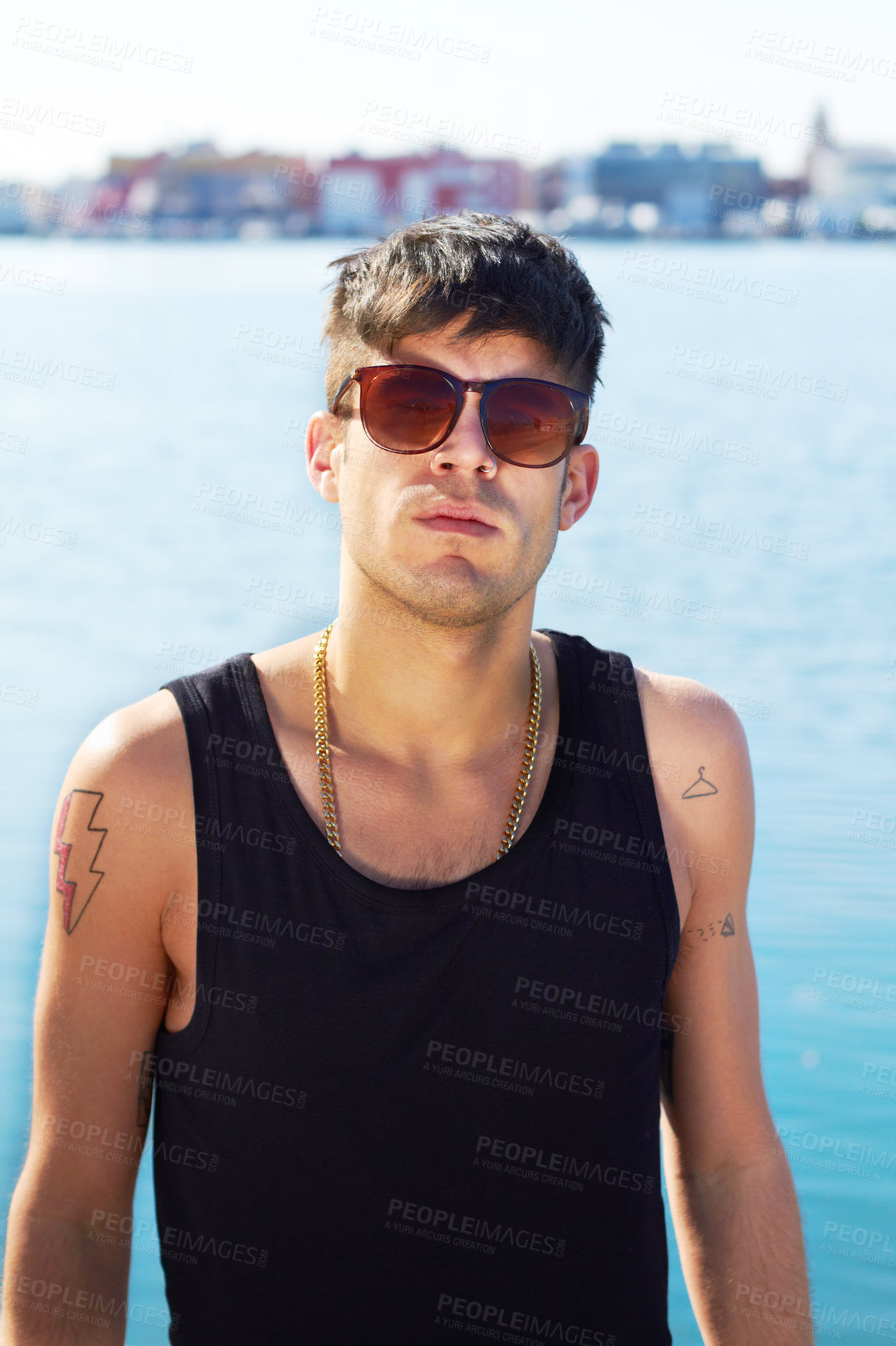 Buy stock photo Portrait, sunglasses and serious man by ocean with stylish tattoo, body art and fashion. Face, sea and trendy male person standing outdoor in Norway with cool clothes, attitude and youth aesthetic.