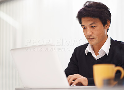 Buy stock photo Shot of a handsome asian businessman working on his laptop in the office