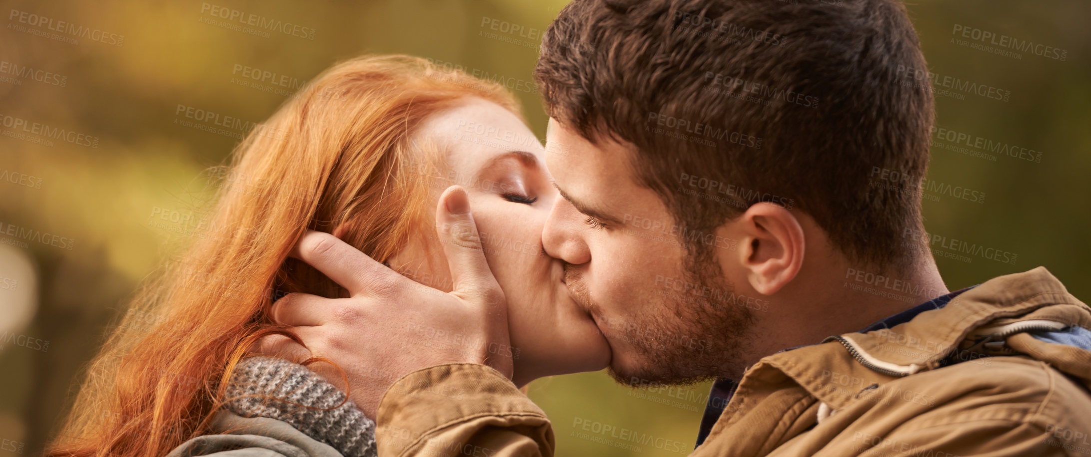 Buy stock photo Shot of a happy young couple sharing a kiss outdoors