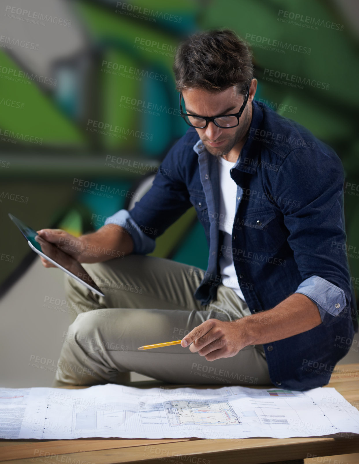 Buy stock photo Shot of a trendy male designer working on building plans at his desk
